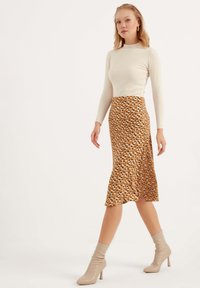 Een aansluitend crèmekleurig langslievend top gecombineerd met een flared midi-rok met een bruin bloemenpatroon, aangevuld met beige hoge hakken.