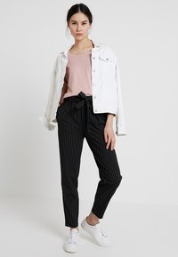Hvit denimjakke over en lys rosa topp, kombinert med svart og hvit stripete bukser og hvite joggesko; en uformell antrekk med løs passform.