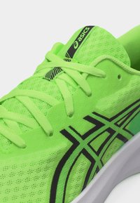 Φωτεινό πράσινο παπούτσι για τρέξιμο ASICS με μαύρες λεπτομέρειες λογότυπου, πράσινα κορδόνια και λευκή σόλα, με κοντινή εικόνα στα κορδόνια και τη γλώσσα.