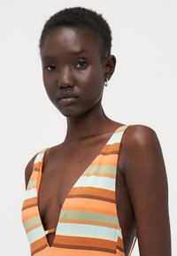 An orange and aqua striped swimwear with a deep V-neck and wide straps, crafted from a textured fabric. Features a cut-out detail.