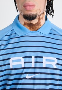 Light blue polo shirt with navy horizontal stripes, featuring a prominent white "AIR" logo and Nike swoosh. Smooth fabric and collar detail.