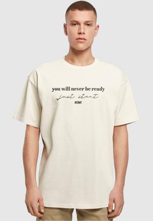 Kremfarget oversized t-skjorte laget av bomull, med svart tekst "du vil aldri være klar, bare start" og hashtag #START.