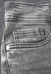 Jean en denim gris avec une poche frontale dotée de coutures détaillées et d'un rivet en métal argenté, présentant une texture délavée et une finition lisse.