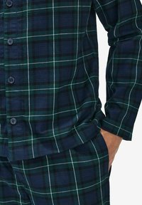 Tumman vihreä ja laivaston sininen ruudullinen puuvillapuku, jossa on napit, pitkät hihat ja rento istuvuus. Kankaassa on teksturoitu, kudottu kuvio.