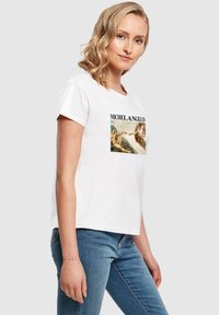 Hvid bomulds t-shirt med et centralt print af et Michelangelo kunstværk, rund hals, korte ærmer og en afslappet pasform sammen med blå jeans.