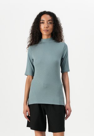 Ribbet, teal t-skjorte med korte ermer og høy hals, sammen med svarte shorts. Glatt tekstur, tettsittende design og sideslisser i kanten.