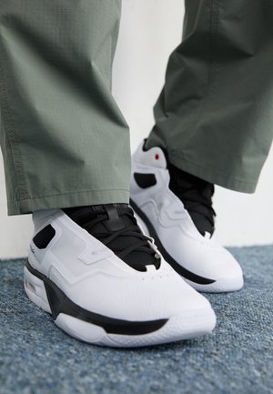 Weiße Sportschuhe mit schwarzen Akzenten, Obermaterial aus strukturiertem Leder, schwarze Schnürsenkel und sichtbare Luftpolstersohle. Getragen mit grüner Hose.