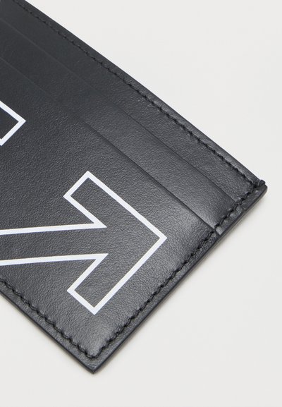 Μαύρος δερμάτινος θήκη καρτών με λευκό περίγραμμα βέλους και πολλαπλές θήκες για κάρτες, απεικονίζεται σε ανοιχτό φόντο.