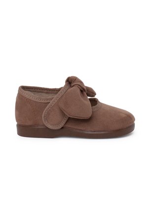 Scarpa in suede marrone con punta tonda, apertura elasticizzata e un grande fiocco decorativo sul lato. Suola piatta in gomma marrone.