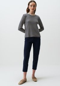Marineblauw en crème gestreepte lange mouwen top met een scalloped halslijn, gecombineerd met marineblauwe cropped broeken en beige loafers, tegen een neutrale achtergrond.