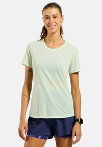 T-shirt de sport en mesh vert clair à manches courtes et col rond, avec un logo tonal sur la poitrine. Texture lisse, design respirant.