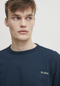 Mornarsko modra bombažna majica s krožnim izrezom, ki ima na prsih izšit majhen logotip "BLEND". Gladka tekstura, sproščen oblikovanje.