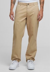 Beige bomullsbukser med rett snitt, frontlommer og metallknapp lukking, parret med hvite joggesko.