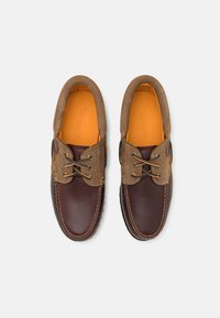 Chaussures en cuir marron avec un accent en daim sur le col, dotées de deux œillets, de détails brodés et d'une semelle intérieure colorée orange.