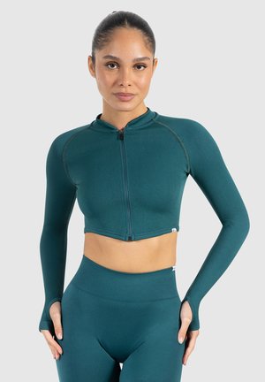 Teal cropped zip-up top met lange mouwen, geribbeld textuur en duimopeningen. Gecombineerd met bijpassende hoge taille leggings.