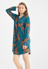 Teal nachthemd met een oranje tijgerprint over de hele stof, lange mouwen, knoopsluiting en een relaxte pasvorm. Zachte stof met een gladde textuur.