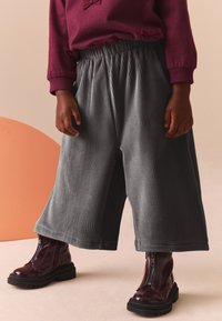 Pantaloni evazați gri din corduroy, cu un brâu elastic, asociați cu cizme scurte lucioase de culoare burgundă, cu fermoar pe lateral.