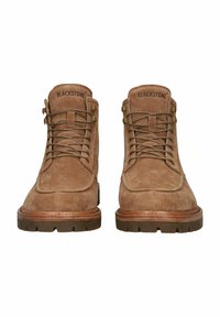 Botas de tobillo de ante marrón con punteras redondeadas, diseño de cordones y suelas de goma. Presentan costuras sutiles y ojales de metal. Marca "BLACKSTONE" en la lengüeta.