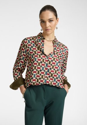 Camisa de seda con un patrón geométrico en burdeos, azul y crema. Presenta un diseño de botones, mangas enrolladas y un cuello.