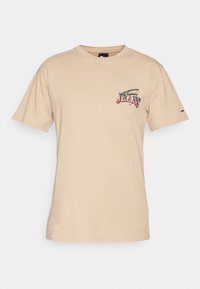 Beige bavlněné tričko s krátkým rukávem, kulatým výstřihem a předním grafickým designem s nápisem "JEANS" v barevném písmu.