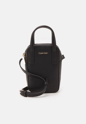 Mała czarna skórzana torebka Calvin Klein z dwoma górnymi uchwytami i regulowanym paskiem na ramię, złotym zamkiem błyskawicznym oraz logo z przodu.