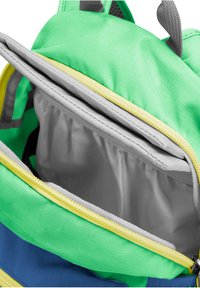 Sac à dos vert et bleu avec une fermeture éclair jaune ouverte pour montrer le compartiment principal vide et une poche intérieure rembourrée grise.