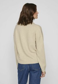 Beige knit sweater with a relaxed fit and dropped shoulders, paired with blue denim jeans, showing a smooth texture and casual design.