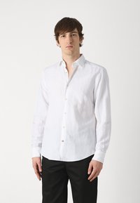 Camicia bianca in lino a maniche lunghe con colletto button-down, caratterizzata da un tessuto leggermente strutturato e piccoli bottoni simili a perle lungo il davanti.