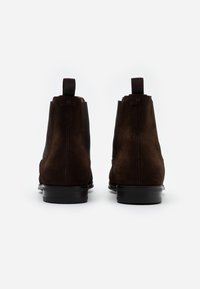 Bottines en daim marron avec panneaux élastiques sur les côtés et languettes de tirage, présentant un bout rond élégant et une semelle en caoutchouc noire.