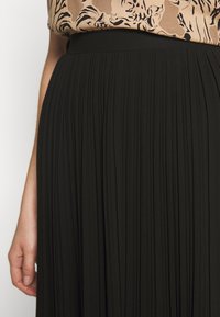 Černá skládací sukně s pružným pasem. Materiál má hladkou texturu a dlouhý volný design dosahující do poloviny lýtek.