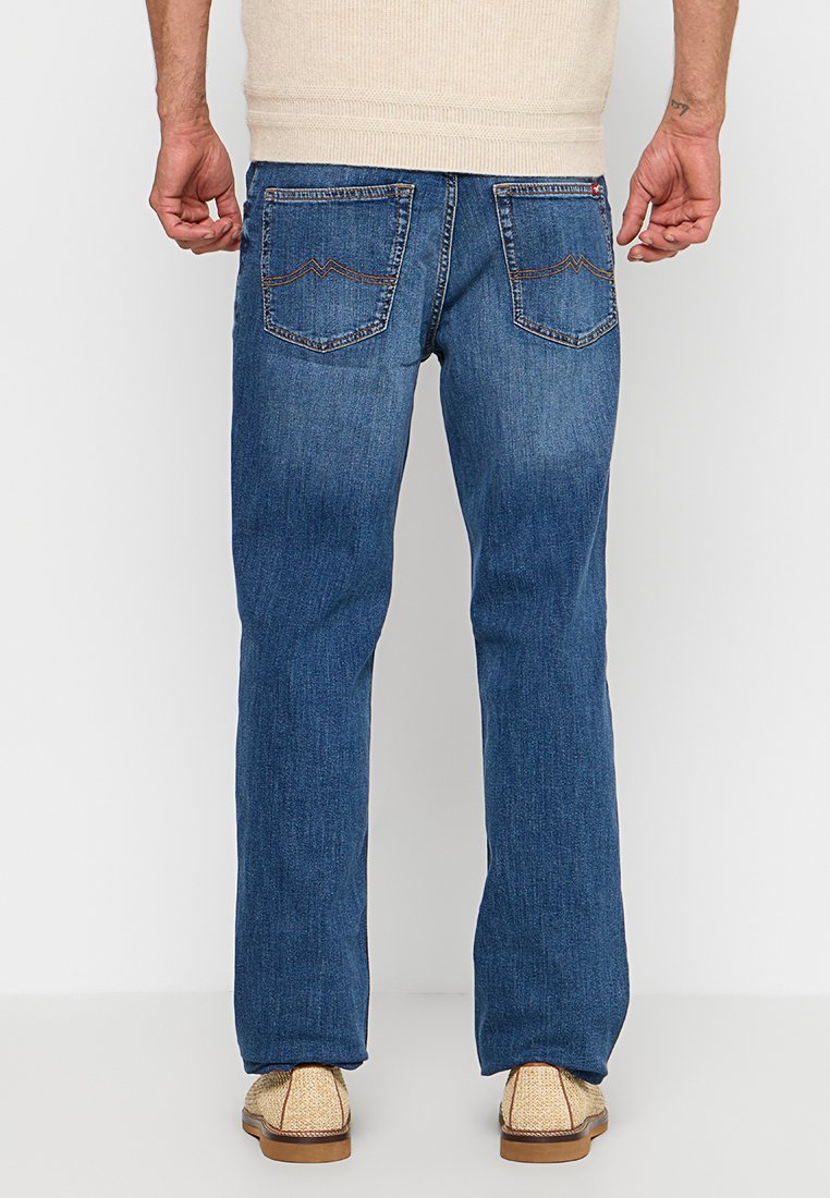 Niebieskie dżinsy z prostą nogawką, z tylnymi kieszeniami o kontrastowym haftowaniu i lekkim przetarciem. Noszone z beżowymi butami.