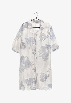 Lehká, průsvitná bílá košile s modrými květinovými vzory, krátkými rukávy a zapínáním na knoflíky vpředu. Visí na černém háčku.