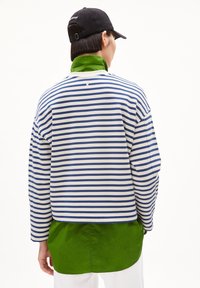 Pullover a righe con strisce orizzontali blu e bianche, caratterizzato da un colletto verde. Indossato sopra una camicia verde, presenta una vestibilità comoda.