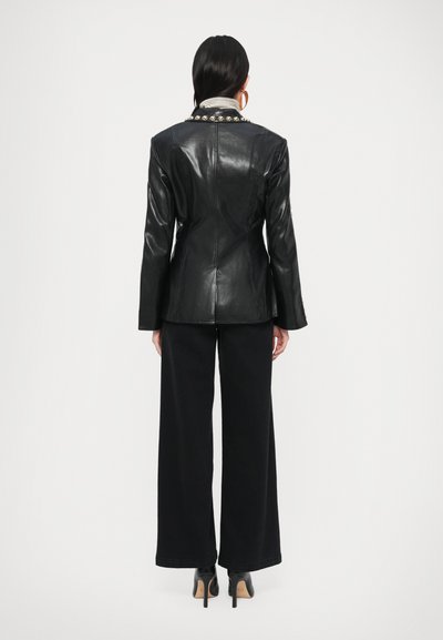 Fekete bőrből készült blézer strukturált szabással, hosszú ujjakkal és ezüst szegecses gallérral, széles szárú fekete nadrág és magassarkú cipő felett viselve.
