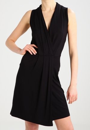 Robe noire sans manches avec un décolleté en V profond, des détails de tissu plissé et un ourlet asymétrique. Fabriquée dans un matériau doux et extensible.