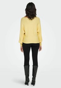 Ż�ółty prążkowany sweter z szerokim dekoltem, długimi rękawami oraz czarne rurki w połączeniu z czarnymi kozakami na obcasie do kolan.
