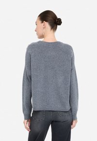Maglione grigio a maglia con dettagli a coste sulle spalle, vestibilità rilassata e scollatura rotonda, abbinato a jeans grigio scuro.