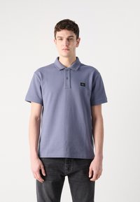 Polo en coton violet clair avec un col, un patte de boutonnage à deux boutons, des manches courtes et un petit patch logo noir sur la poitrine.