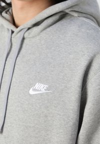 Grå hoodie i mjukt material med en känguruficka, prydd med en vit Nike-logotyp på bröstet och matchande snören.
