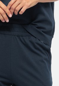 Granatowa bawełniana bluzka z krótkimi rękawami, w połączeniu z dopasowanymi spodniami w luźnym kroju. Widoczny elastyczny pas i detal w szwie bocznym.