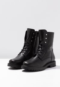Bottines en cuir noir avec un laçage à l'avant, fermeture éclair sur le côté, bout rond, semelle en caoutchouc avec des crampons, et accents décoratifs en métal argenté.