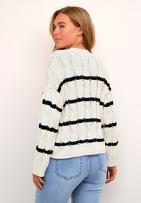 Pulover alb tricotat cu dungi orizontale negre, prezentând un model texturat și tiv cu nervuri. Purtați cu blugi bleu deschis.
