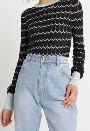 Zwart-wit top met lange mouwen en patroon, gecombineerd met een lichtblauwe spijkerbroek met hoge taille.