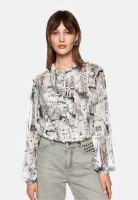 Durchsichtige Bluse mit einem monochromen Stadtlandschaftsprint, ausgestattet mit einem Rüschenausschnitt, einem Knopf-Schlüsselloch und langen, gepufften Ärmeln; kombiniert mit grauen Jeans.