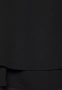 Black textured fabric with a smooth finish. Features a curved hem and clean stitching. No visible patterns or embellishments.