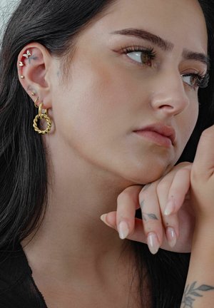 Goldene Creolen mit einem verdrehten Design, verziert mit mehreren kleinen Nieten am Ohrläppchen und einer glatten Oberflächenstruktur.