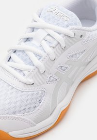 White athletic shoe featuring a textured mesh upper, tonal grey accents, and a bright orange rubber sole. Includes white laces and branding.