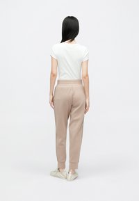 Μπεζ φόρμα με τελειώματα στα μπατζάκια και πλαϊνές λεπτομέρειες, συνδυασμένη με εφαρμοστή λευκή μπλούζα, σε θέα από πίσω σε ουδέτερο φόντο.