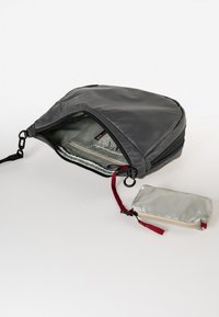 Zaino grigio con una finitura liscia e opaca; include una tasca interna e una piccola pochette argentata con una cerniera rossa e una tracolla.