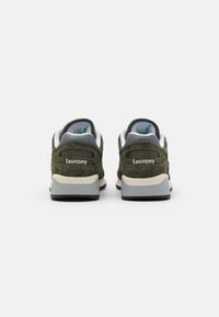 Zelené semišové tenisky s bielymi akcentmi, obsahujúce polstrovaný golier, tmavosivú podrážku a logo "Saucony" na päte.